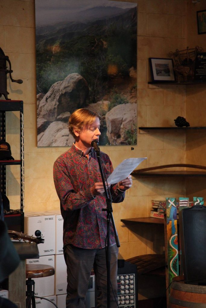 Author and artist Max Talley reading at a microphone.